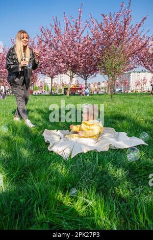 Mère et fils joyeux jouant avec des bulles près des cerisiers en fleurs. Banque D'Images