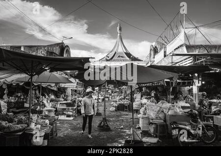 Une cabas femme portant un casque d'accident et un masque facial marche à travers une zone du marché central de Pleiku, dans les Highlands centraux du Vietnam. Banque D'Images