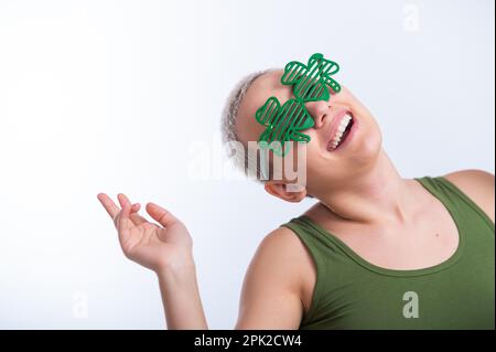 Portrait d'une jeune femme caucasienne avec une coupe de cheveux d'un homme dans un t-shirt vert et des lunettes gaies sur un fond blanc. La jeune fille célèbre St patrick Banque D'Images