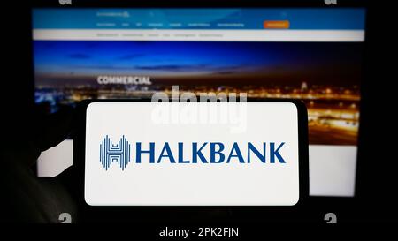 Personne tenant un téléphone portable avec le logo de la société Turkiye Halk Bankasi A.S. (Halkbank) à l'écran en face de la page Web. Mise au point sur l'affichage du téléphone. Banque D'Images