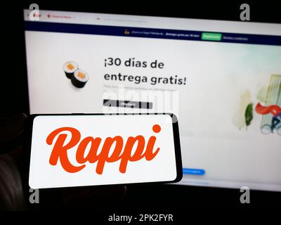 Personne tenant un téléphone portable avec le logo de la compagnie colombienne de livraison de nourriture Rappi Inc. À l'écran en face de la page Web. Mise au point sur l'affichage du téléphone. Banque D'Images