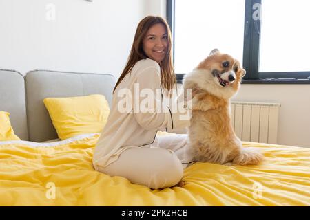 une jeune fille avec un chien corgi joue sur le lit et une journée lumineuse dans la chambre, la vie avec un chien, un ami d'une personne Banque D'Images