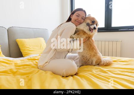 une jeune fille avec un chien corgi joue sur le lit et une journée lumineuse dans la chambre, la vie avec un chien, un ami d'une personne Banque D'Images