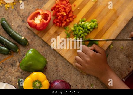 Les mains de jeunes afro-américaines hacher des poivrons sur la planche à découper dans la cuisine Banque D'Images