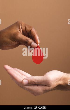 Mains de l'homme biracial donnant une goutte de sang à l'homme caucasien, sur fond marron Banque D'Images