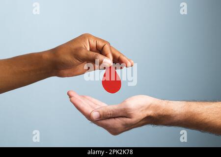 Mains de l'homme biracial donnant une goutte de sang à l'homme caucasien, sur fond bleu Banque D'Images