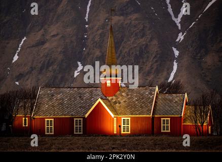 Église en bois de couleur rouge à partir de 1780 ans, illuminée le soir avec une haute montagne rocheuse avec de la neige. Église Flakstad, Lofoten, Norvège. Banque D'Images