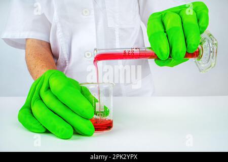 Un médecin scientifique verse du liquide rouge (sang) d'une éprouvette dans un bécher dans le laboratoire Banque D'Images