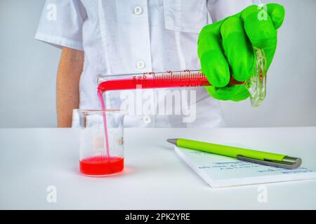 Un médecin scientifique verse du liquide rouge (sang) d'une éprouvette dans un bécher dans le laboratoire Banque D'Images