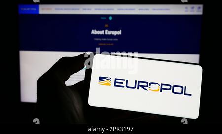 Personne tenant un téléphone portable avec le logo de l'agence européenne chargée de l'application de la loi Europol à l'écran devant la page Web. Mise au point sur l'affichage du téléphone. Banque D'Images