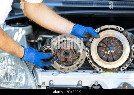 Ouvrier automobile tenant un disque d'embrayage, un plateau de pression et un palier de débrayage usagés devant le moteur du véhicule Banque D'Images