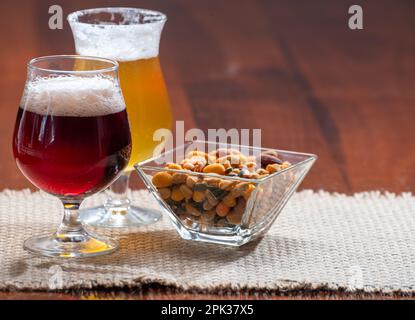 Verres de bière blonde jaune belge et marron foncé faits à l'abbaye servis au bar avec noix de fête, gros plan Banque D'Images