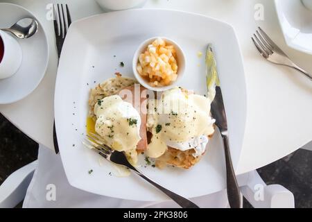 Oeufs benedict petit déjeuner sur une assiette blanche et une table avec de l'argenterie Banque D'Images