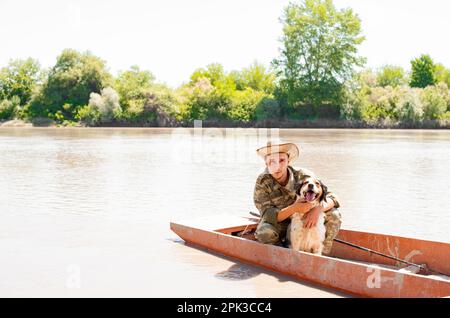 Propriétaire masculin souriant, pêcheur embrassant un chien déchiquable, posant à la caméra, tout en étant assis en bateau pendant les vacances. Banque D'Images