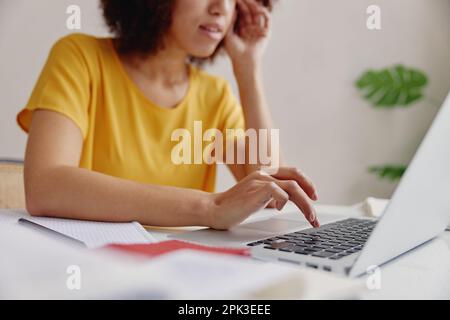 Vue partielle de la jeune femme afro-américaine assise au bureau et dactylographiant sur un ordinateur portable au bureau. Banque D'Images