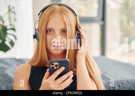 Dans les écouteurs. Une adolescente avec des cheveux blonds est à la maison le jour Banque D'Images