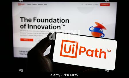 Personne tenant un smartphone avec le logo de la société de logiciel d'automatisation UiPath Inc. À l'écran devant le site Web. Mise au point sur l'affichage du téléphone. Banque D'Images