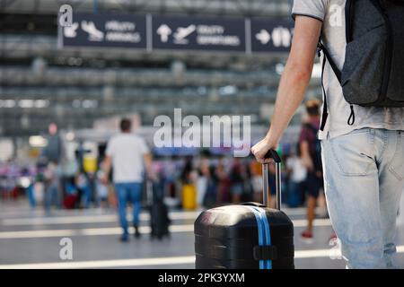 Voyager en avion. Attention sélective à la main de l'homme tenant la valise. Les voyageurs qui voyagent avec leurs bagages à travers le terminal de l'aéroport vers l'enregistrement. Banque D'Images