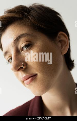 gros plan portrait d'une jeune femme à l'état de taches de rousseur avec perçage du nez regardant la caméra isolée sur image grise Banque D'Images