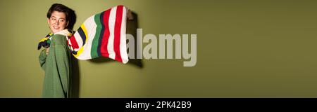 femme surjoyeuse dans un pull tendance et foulard rayé agitant sur le vent sur fond vert, bannière, image de stock Banque D'Images