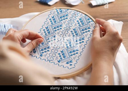 Femme brodant une chemise blanche avec fil bleu sur une table en bois, gros plan. Vêtements nationaux ukrainiens Banque D'Images