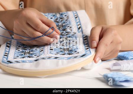 Femme broderie avec fil bleu à la table, gros plan. Vêtements nationaux ukrainiens Banque D'Images