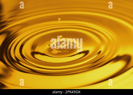 Éclaboussures de liquide huileux doré avec des gouttes comme arrière-plan, gros plan Banque D'Images