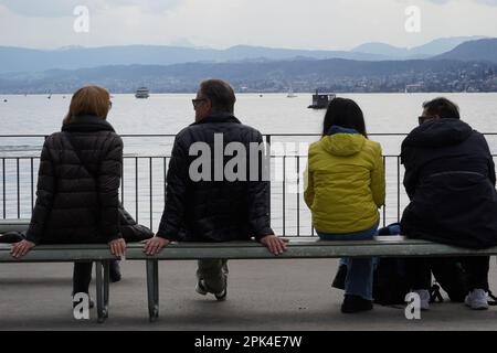 Deux couples hétérosexuels assis sur un banc sur la rive du lac de Zurich. Vue arrière avec le lac et les Alpes suisses en arrière-plan. Banque D'Images