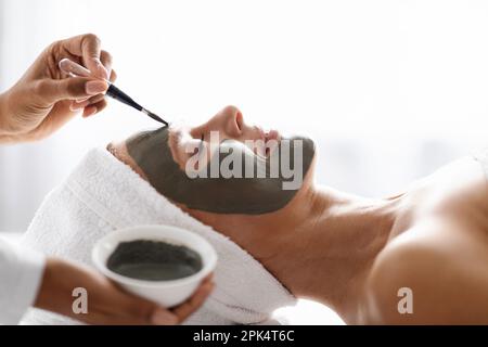 Soins de la peau anti-âge. Cosmétologue appliquant le masque sur le visage de la belle femme d'âge moyen Banque D'Images