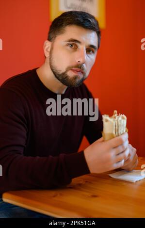 Un homme avec une barbe est assis sur une chaise et de manger le shawarma, une collation rapide, savoureuse et saine dans un restaurant de restauration rapide. Banque D'Images