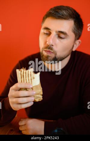 Un homme avec une barbe est assis sur une chaise et de manger le shawarma, une collation rapide, savoureuse et saine dans un restaurant de restauration rapide. Banque D'Images