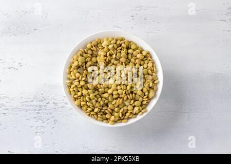 Lentilles crues trempées dans un bol blanc sur fond gris clair, vue du dessus. Concept d'alimentation saine Banque D'Images