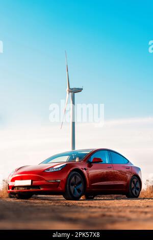 Vue sur une voiture électrique rouge garée. Éolienne en arrière-plan Banque D'Images