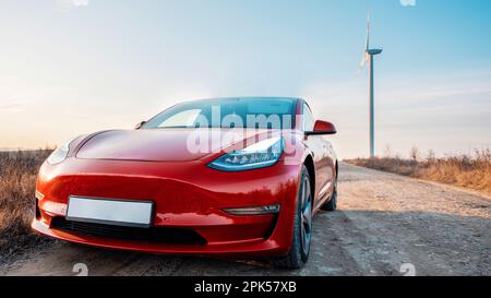 Vue sur une voiture électrique rouge garée. Éolienne en arrière-plan Banque D'Images