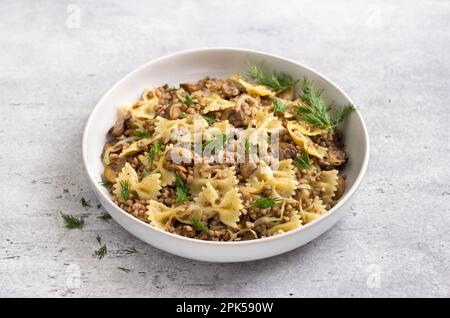 Plat traditionnel juif kasha vernis: Sarrasin, pâtes, champignons champignon, oignons frits aux herbes sur fond gris texturé, nourriture végétalienne, t Banque D'Images