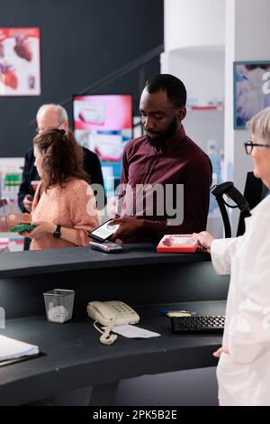 Pharmacie client debout au comptoir de pharmacie mettre téléphone sur le terminal de pos payer les pilules prescription avec le téléphone moderne, l'achat de vitamines et de suppléments. Services et soutien en matière de soins de santé Banque D'Images