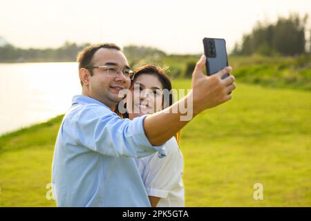 Couple d'amoureux romantiques prenant le selfie avec parc vert dans la soirée Banque D'Images