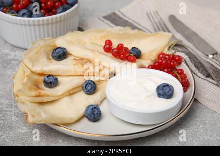 Crêpes délicieuses avec yaourt naturel, bleuets et raisins de Corinthe rouges sur table grise Banque D'Images