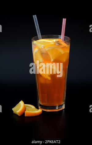 Limonade d'orange rafraîchissante avec glace, tranches d'agrumes et pailles dans un grand verre à facettes sur fond noir. Disposition verticale. Banque D'Images