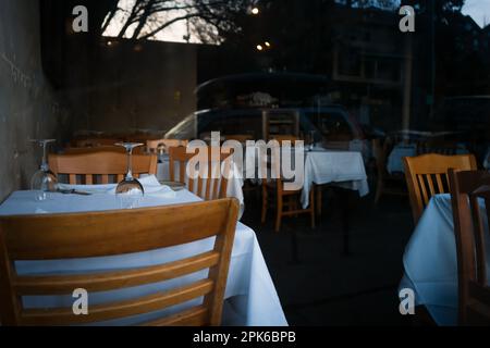 La salle à manger du restaurant est vide, l'éclairage est éteint. Nappe blanche, chaises en bois, verres à vin Banque D'Images