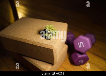 Une photo en gros plan d'une fleur de marijuana placée sur deux blocs de yoga en liège, à côté des haltères Banque D'Images