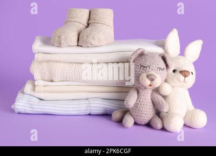 Pile de vêtements pour bébés, chaussettes et jouets tricotés sur fond lilas Banque D'Images