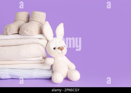 Pile de vêtements, chaussettes et tricoté pour bébé sur fond lilas Banque D'Images