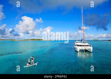 Les femmes paddle SUP et font du yoga devant un catamaran dans le port de Warderick Wells, aux Bahamas et dans le parc national d'Exuma Cays Land and Sea Banque D'Images