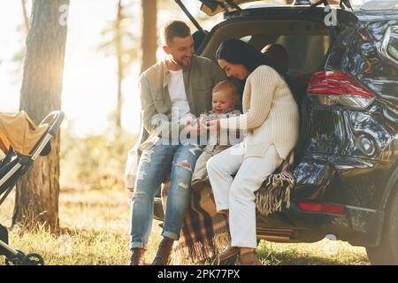 Assis à l'arrière de l'automobile. Une famille heureuse de père, de mère et de petite fille est dans la forêt Banque D'Images