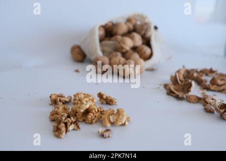 Cerneaux de noyer, coquillages de noyer et un sac en tissu blanc rempli de noix entières sur un fond de table blanc. Idée de photo de concept de noix cassées fissurées. Banque D'Images