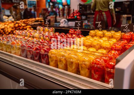 Salade de fruits disposée dans des tasses en plastique sur un marché avec une petite fourchette à l'intérieur, en-cas à emporter. Nourriture dans le supermarché.Barcelona, ​​Spain Banque D'Images