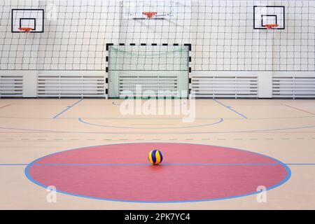 Une salle de sport d'école avec un terrain de football intérieur marqué, des paniers de but et de basket-ball, une balle rayée bleue et jaune dans un cercle rose. Banque D'Images