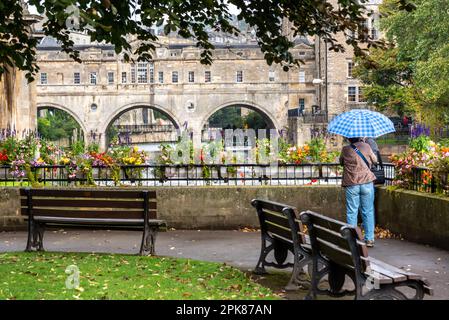 Hommes tenant un parapluie face au pont de Pulteny à Bath, Royaume-Uni Banque D'Images