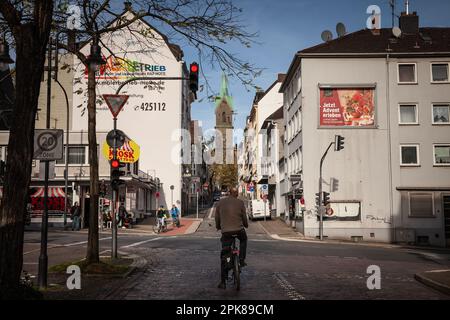 Photo d'un homme à vélo, attendant de traverser une rue où les voitures sont en voiture à Wuppertal, en Allemagne, avec l'église diakoniekirche en arrière-plan. Banque D'Images